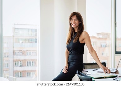 Full length shot of attractive businesswoman wearing black dress while standing at desk in a modern office. 