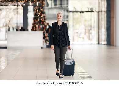 Full length shot of an attractive mature businesswoman pulling a suitcase while walking through an airport terminal during the day