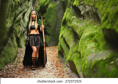 Full length shot of a beautiful blonde haired young woman elf wearing a green cape standing in the forest near an old rock copyspace weapon archer archery warrior myth legend hero costume sexy girl.