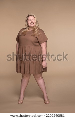 full length shot of beautiful plus size woman in her 20s posing with confidence on neutral background