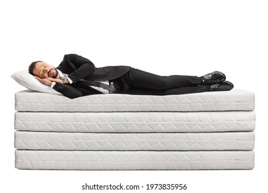 Full length shot of a businessman in a suit and tie sleeping on a pile of mattresses isolated on white background - Powered by Shutterstock