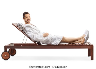 Full length shot of a cheerful young man in a bathrobe relaxing on a lounge chair and smiling at the camera isolated on white background