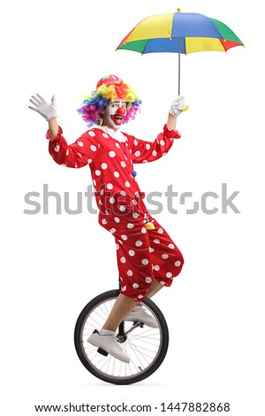 Full length shot of a clown riding a unicycle and holding an umbrella isolated on white background