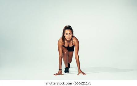 Full Length Shot Of Confident Female Athlete In Start Position Ready For A Run. Hispanic Young Woman About To Start A Sprint Over Grey Background.