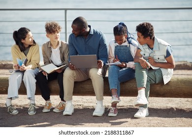 Full Length Shot Of Diverse Group Of Kids With Male Teacher Using Laptop Outdoors During Summer School Lesson