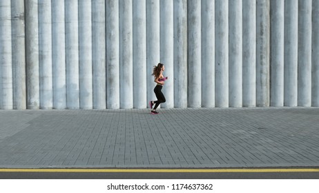 Full length shot of fit young woman jogging in the street. Fitness model exercising in morning outdoors. Healthy lifestyle concept