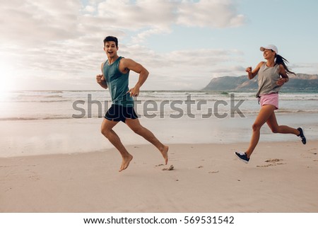 Full length shot of fit young man and woman running on the beach. Happy young couple of runners on the sea shore.