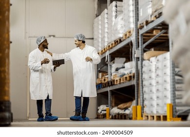 Full length shot of food plant warehouse workers with tablet walking towards camera and talking. Team of two diverse food factory workers collaborating - Powered by Shutterstock