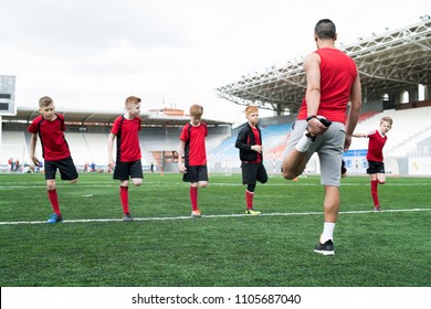 Full length shot of  football coach showing stretching exercises to group of boys during warm up before practice in outdoor stadium - Powered by Shutterstock