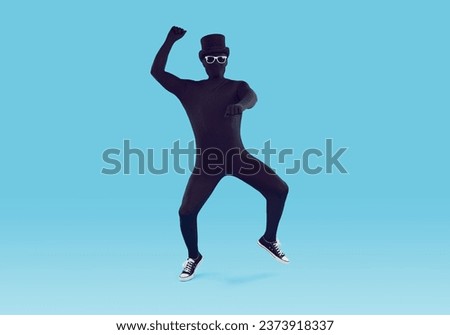 Full length shot of a funny man disguised in a black skin tight spandex bodysuit costume, sunglasses, top hat and trainers dancing gangnam style isolated on a blue colour background