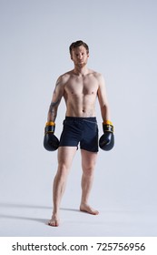 Full Length Shot Of Good Looking Barefooted Young Male Model With Thick Beard And Perfect Muscular Body Wearing Boxing Gloves And Trunks Posing In Studio During Photoshooting For Sports Magazine.