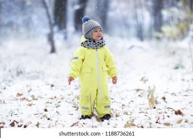 Full Length Shot Of Happy Boy In Yellow Snowsuit Standing In Snowy Park