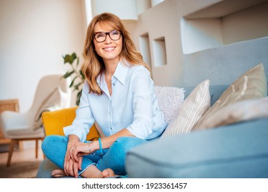 Full length shot of happy mature woman relaxing on couch at home while looking thoughtfully.