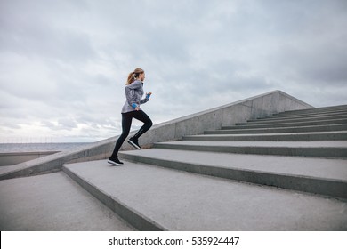 Full Length Shot Of Healthy Woman Climbing Up On Stairs. Fitness Female Exercising Outdoors In Morning.