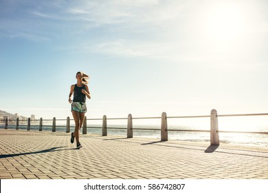 Full length shot of healthy young woman running on the sea side promenade. Female runner working out on a sunny morning. - Powered by Shutterstock