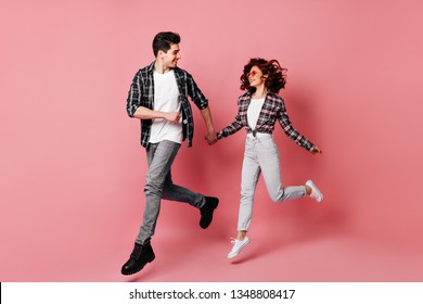 Full Length Shot Of Jumping Couple Having Fun Together. Studio Photo Of Young People Running On Pink Background.