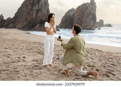 Full length shot of loving man with engagement ring proposing to surprised lady, guy standing on knee on ocean beach, free space. Love is in the air - Powered by Shutterstock