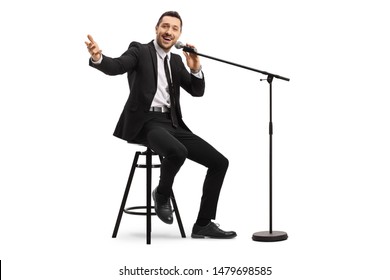 Full Length Shot Of A Male Singer Sitting On A Chair And Holding A Microphone On A Stand Isolated On White Background