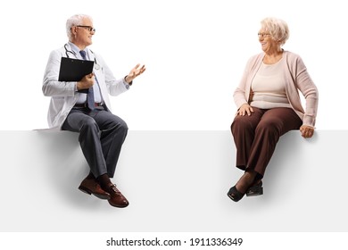 Full Length Shot Of A Mature Doctor Sitting On A Blank Panel And Talking To An Elderly Female Patient Isolated On White Background