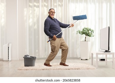 Full Length Shot Of A Mature Man Dancing With A Cleaning Mop In Front Of Tv And Looking At Camera