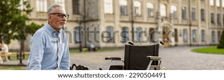 Full length shot of mature recovering patient with wheelchair sitting on the bench in the park near clinic