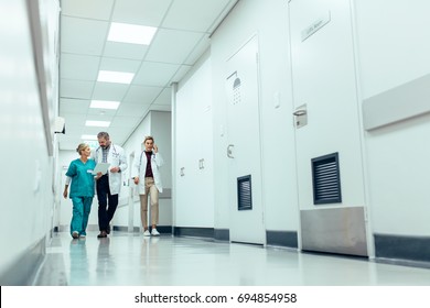 Full Length Shot Of Medical Team Walking Down Hallway At The Hospital. Doctors With Nurse Walking In Hospital Corridor And Discussing.