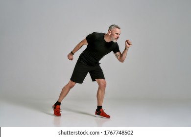 Full Length Shot Of Middle Aged Muscular Man In Black Sportswear Looking Aside While Exercising In Studio Over Grey Background. Sport, Healthy Lifestyle Concept. Horizontal Shot