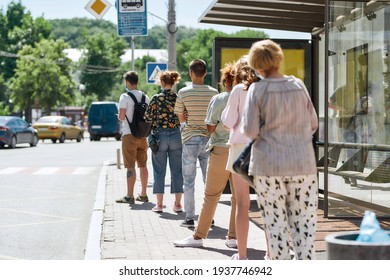 Full length shot of people wearing masks waiting, standing in line, keeping social distance at bus stop. Coronavirus, pandemic concept. Selective focus on guy in the queue. Horizontal shot