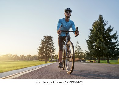 Full length shot of professional male cyclist in sportswear and protective helmet riding road bike in the park at sunset - Powered by Shutterstock