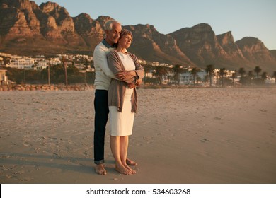 Full length shot of romantic senior couple embracing on the sea shore.  Loving senior couple enjoying the sunset view at the beach.