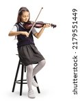 Full length shot of a schoolgirl sitting on a chair and playing a violin isolated on white background