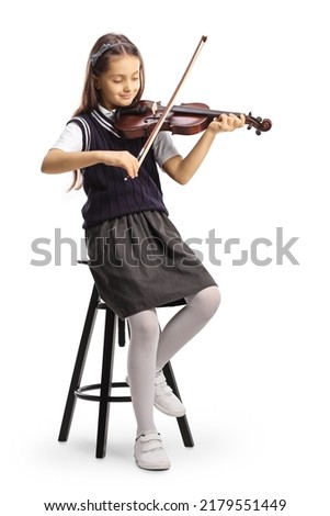 Full length shot of a schoolgirl sitting on a chair and playing a violin isolated on white background