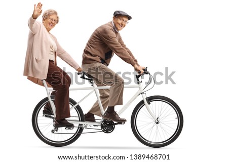 Full length shot of a senior woman and man riding a tandem bycicle and waving isolated on white background