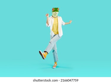 Full Length Shot Of Strange Woman In Funny Animal Disguise Having Fun In Studio. Full Body Portrait Of Happy Young Girl Wearing Green Frog Mask Dancing And Jumping Isolated On Turquoise Background