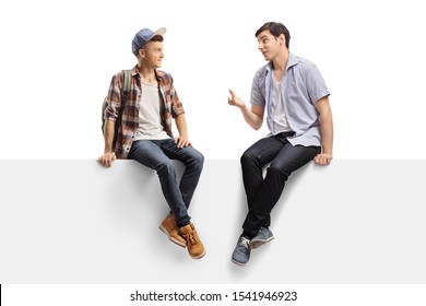Full length shot of two young men sitting on a panel and talking isolated on white background