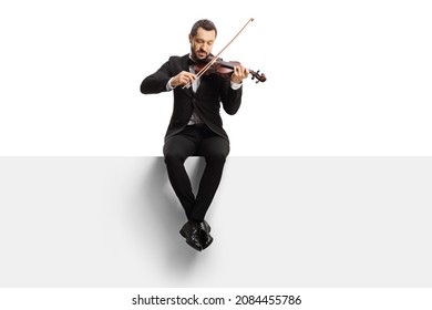 Full length shot of a violinist sitting on a blank panel and playing a violin isolated on white background 