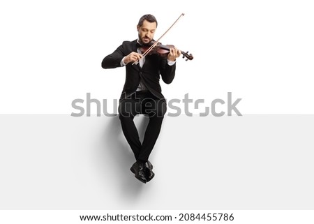 Full length shot of a violinist sitting on a blank panel and playing a violin isolated on white background 