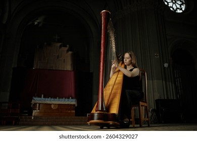 Full length shot of virtuoso female musician delicately playing harp during classical music performance in church with exceptional acoustics, copy space