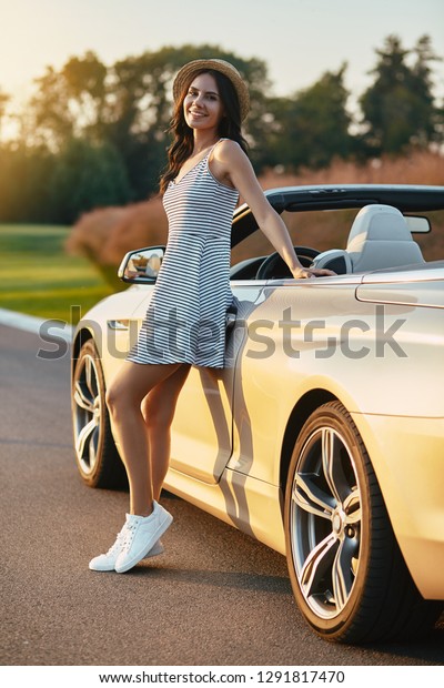 full length shot of woman standing at the car\
and looking at the camera\
outdoors