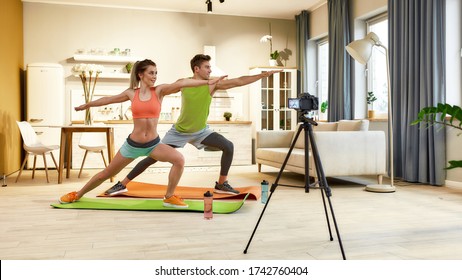 Full length shot of young couple in sportswear recording video blog or vlog about healthy lifestyle on camera while doing yoga at home. Fitness, workout and vlogging concept. Horizontal shot