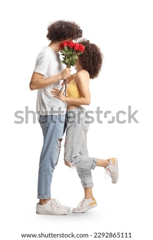 Full length shot of young couple kissing and hiding behinf a bunch of red roses isolated on white background
