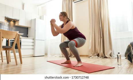 Full Length Shot Of Young Curvy Woman In Sportswear Exercising Using Resistance Band At Home. Determination, Will Power, Sport Concept. Horizontal Shot