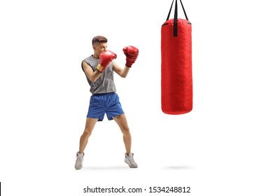 Full Length Shot Of A Young Guy Punching With Boxing Gloves In A Red Hanging Bag Isolated On White Background