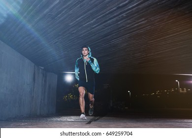 Full length shot of a young man jogging at night. Fit male athlete running under a bridge. - Powered by Shutterstock