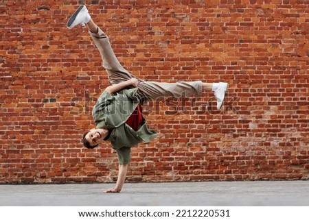 Full length shot of young man doing hip-hop handstand pose and smiling at camera against brick wall, copy space