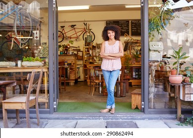 Full length shot of a young mixed race woman happily standing in the doorway of her trendy coffee shop