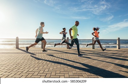 Full length shot of young people running along seaside. Group of runners working out on a road by the sea. - Powered by Shutterstock