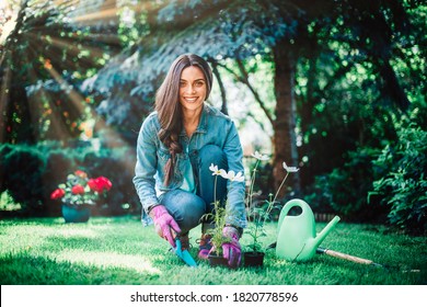 Full Length Shot Of Young Woman Gardening At Home In The Backyard. Happy Woman Wearing Casual Clothes While Planting Flowers.