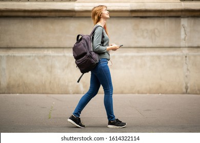 Full length side portrait of happy young woman walking with mobile phone and bag in city - Powered by Shutterstock