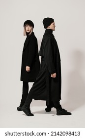 Full Length Side Portrait Of A Millenial Young Man And Woman Walking In Different Directions, Wearing Black Clothes, Hats On White Background With Copy Space